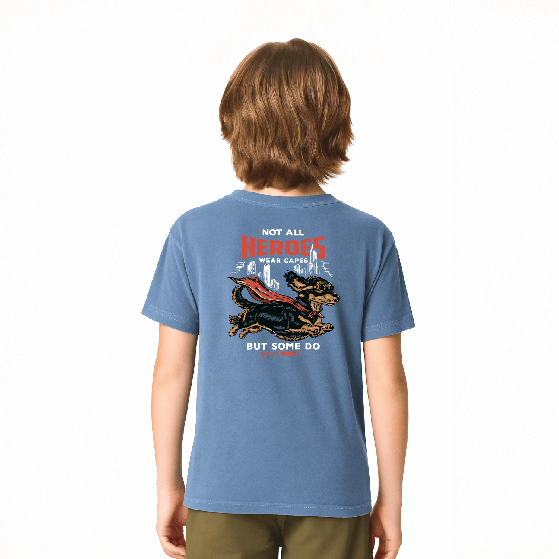 Child wearing a blue washed denim tee featuring a dog in a cape with the text 'Not All Heroes Wear Capes'.