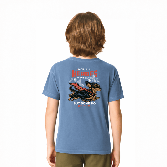 Child wearing a blue washed denim tee featuring a dog in a cape with the text 'Not All Heroes Wear Capes'.
